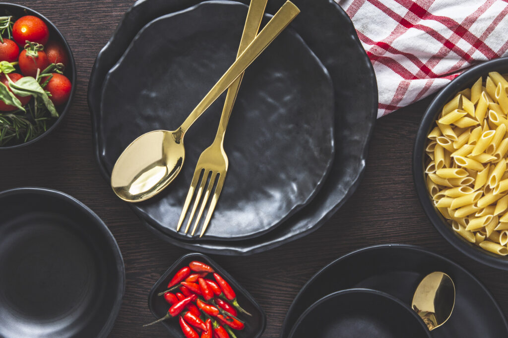 Black dinner crockery with pasta, cherry tomatoes and golden cutlery